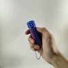 A hand holds a blue and purple 3D printed spike roller fidget toy with a silver keychain.