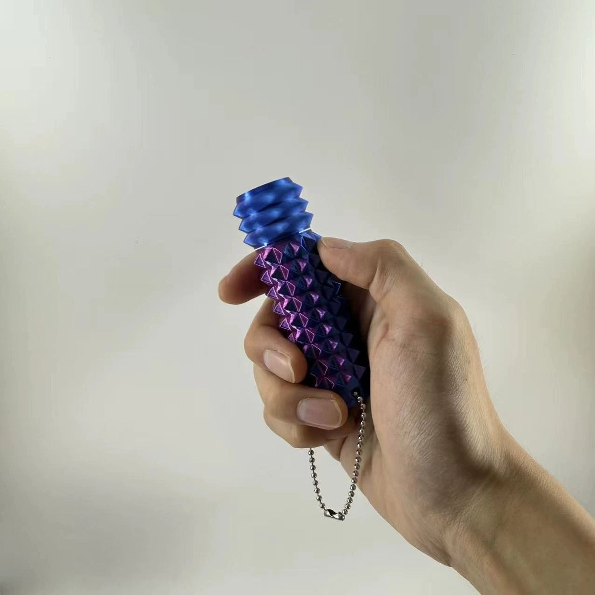 A hand holds a blue and purple 3D printed spike roller fidget toy with a silver keychain.
