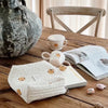 A quilted white baby diaper caddy organizer with small animal figures rests on a wooden table.