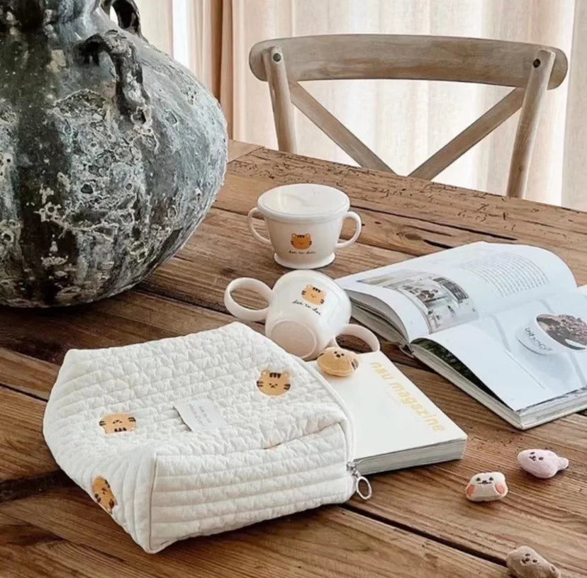 A quilted white baby diaper caddy organizer with small animal figures rests on a wooden table.