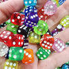 A hand holds a collection of colorful transparent dice in various shades of red, green, purple, and pink.