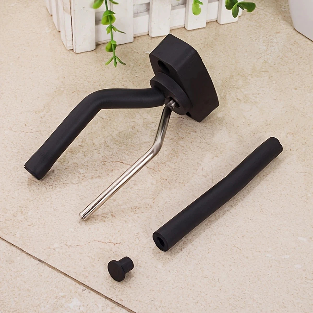 A black universal guitar wall mount hanger with a curved arm and a cylindrical rod is shown on a light surface.