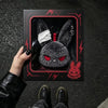 A dark gray gothic bunny plush keychain with a white bandage design is displayed against a black background.