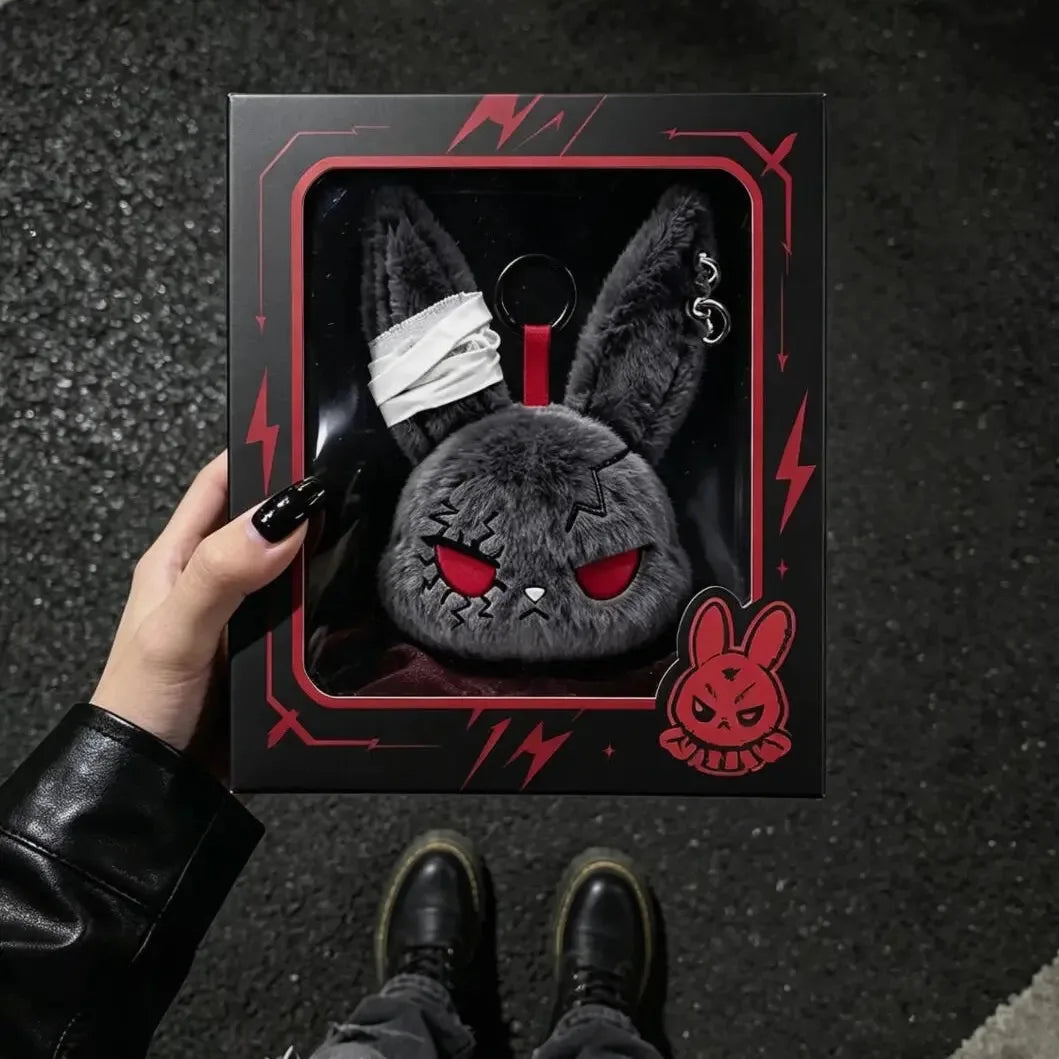 A dark gray gothic bunny plush keychain with a white bandage design is displayed against a black background.