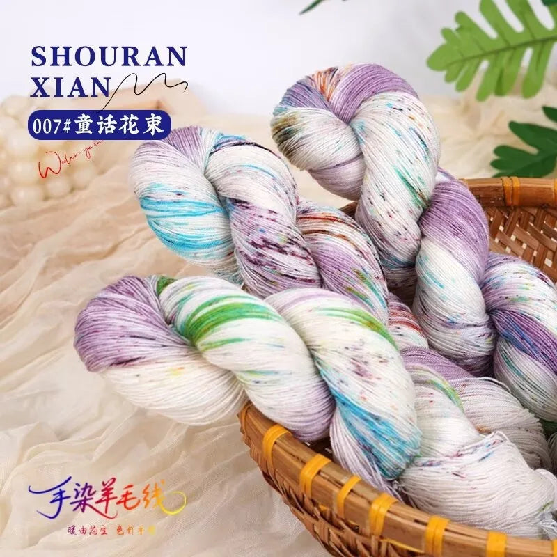 A bundle of hand-dyed wool yarn in a gradient of purple, blue, and white is displayed in a woven basket.
