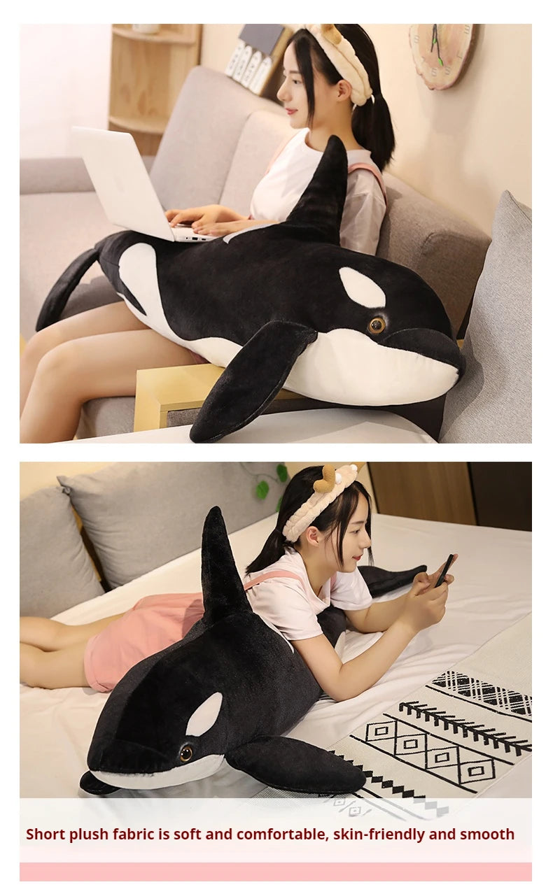 A black and white lifelike orca whale plush toy is shown being held by a woman in a cozy indoor setting.