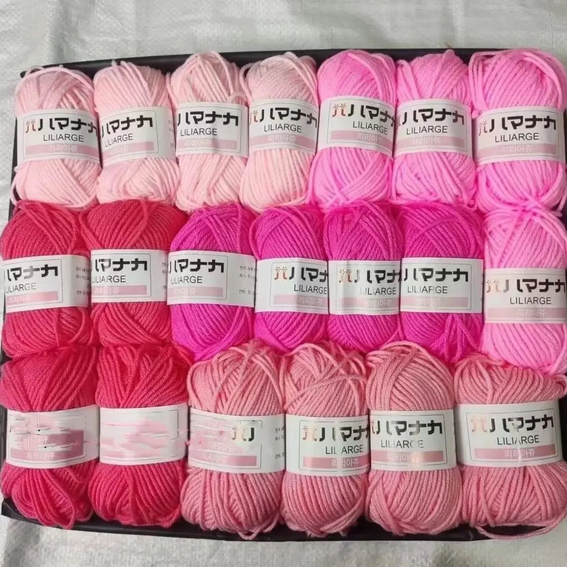 A pack of pink and coral colored acrylic yarn skeins for knitting and crochet crafts.
