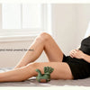 A woman is relaxing in bed using a green neck and shoulder massager for tension relief.