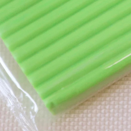 A close-up of a bright lime green polymer clay block with ribbed texture resting on a white surface.