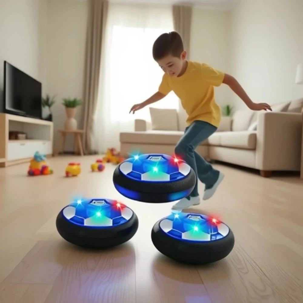 A young boy is playing with glowing LED hover soccer balls on a wooden floor.