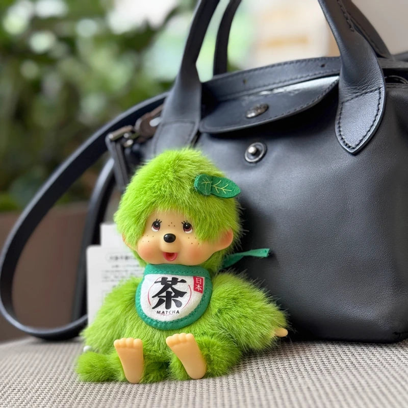 A bright green plush cartoon character with a leaf detail resting on a dark leather handbag.