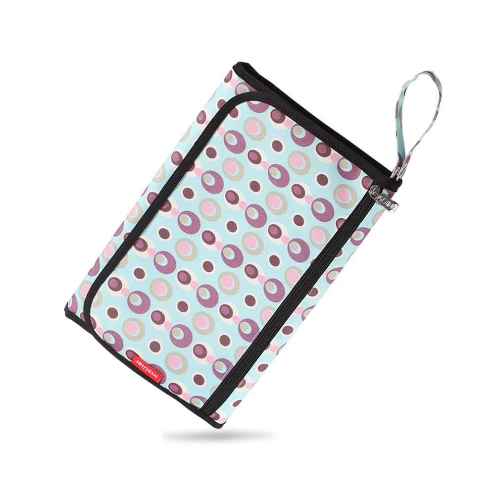A pink and blue patterned portable baby changing mat with a zippered storage bag and carrying strap.