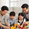 A family is playing with a yellow and blue magnetic train set on the floor, demonstrating parent-child interaction.