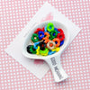 A white bowl filled with colorful acrylic beads featuring floral edges, resting on a card.