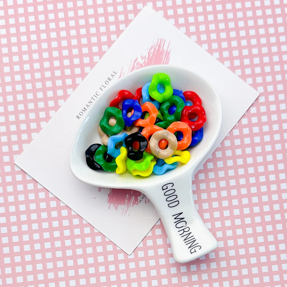 A white bowl filled with colorful acrylic beads featuring floral edges, resting on a card.