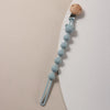 A light blue silicone bear paw pacifier clip with a wooden top and a flexible silicone tube.