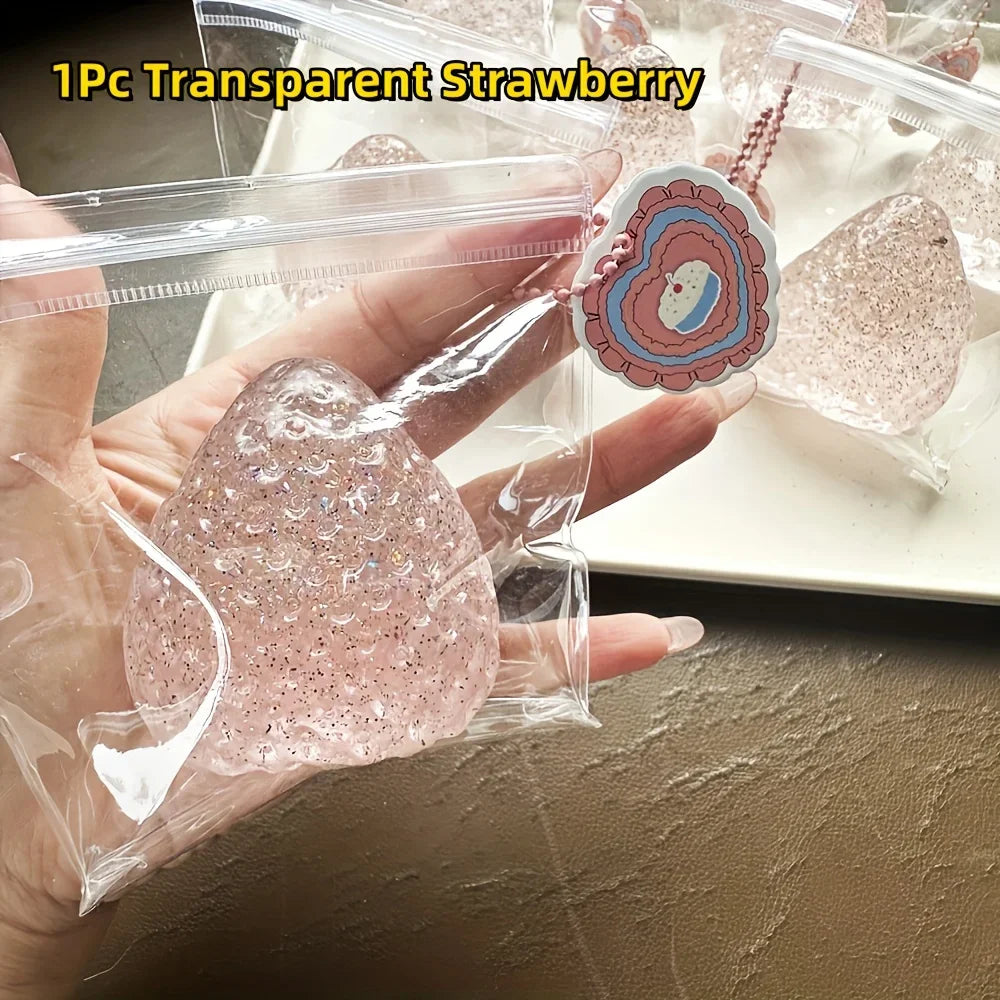 A hand holds a clear plastic bag containing a pink glitter strawberry squishy fidget toy and a heart-shaped charm.