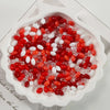 A pile of oval glass rice grain beads in red and white colors displayed in a white dish.