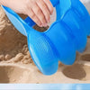 A hand is using a blue dinosaur claw sand digging toy to dig in sand.