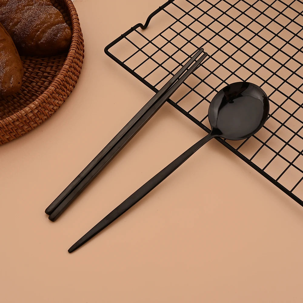 A black stainless steel Korean dinnerware set including chopsticks and a spoon placed on a black wire rack.