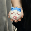 A small plush charm featuring a blue top and white body with pink floral details, held in a person's hand.