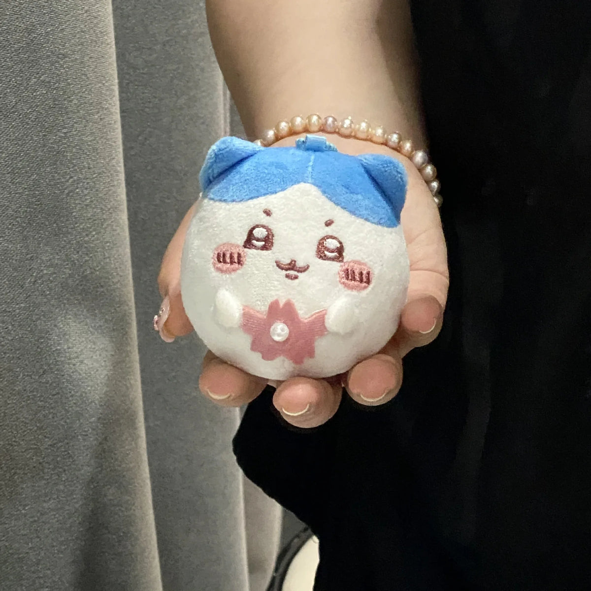 A small plush charm featuring a blue top and white body with pink floral details, held in a person's hand.