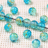 A string of bright blue gradient crystal glass beads with a golden crackle finish resting on a white textured surface.