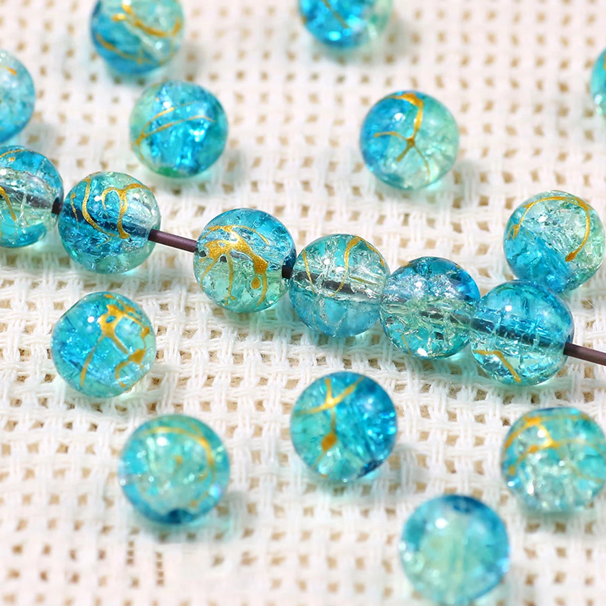 A string of bright blue gradient crystal glass beads with a golden crackle finish resting on a white textured surface.