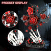 A dark metal cross sculpture featuring red roses and white skeleton hands, displayed against a dark background.
