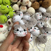A hand holds a variety of handcrafted crochet animal keychains including rabbits, chicks, and cats in various pastel and eart