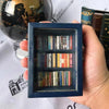A hand holds a dark blue wooden miniature bookshelf ornament filled with small books.