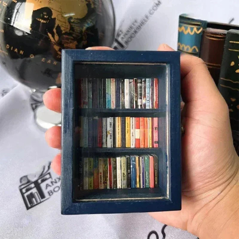 A hand holds a dark blue wooden miniature bookshelf ornament filled with small books.
