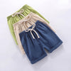 A stack of three kids cotton-linen summer shorts in shades of green, beige, and navy blue.