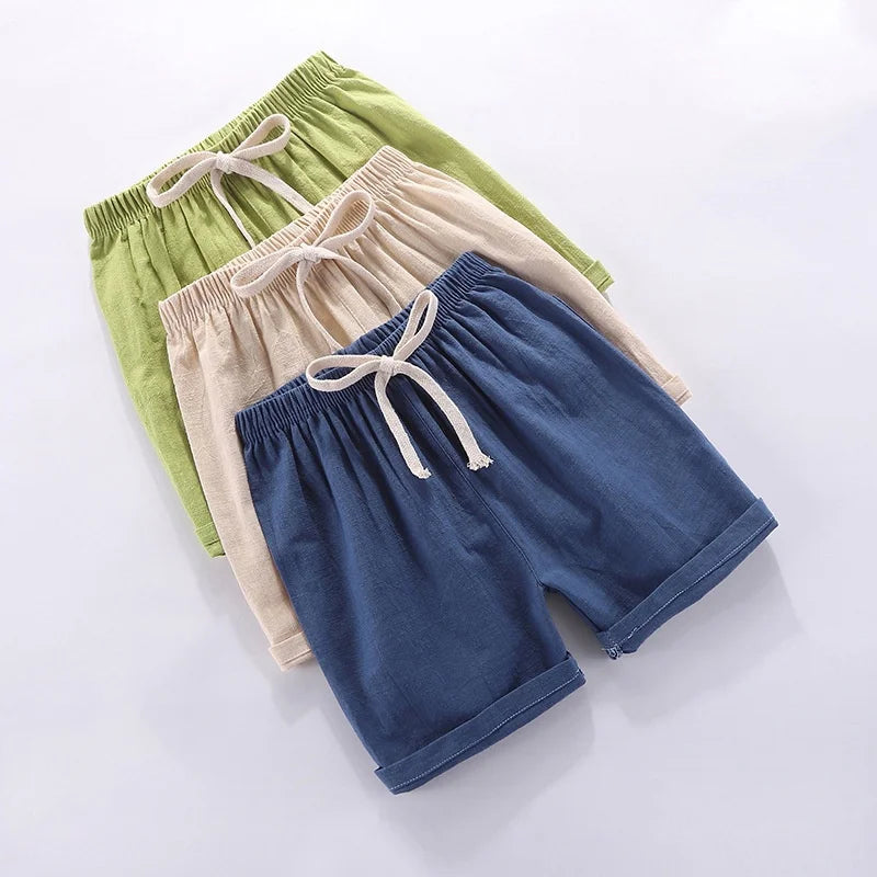 A stack of three kids cotton-linen summer shorts in shades of green, beige, and navy blue.