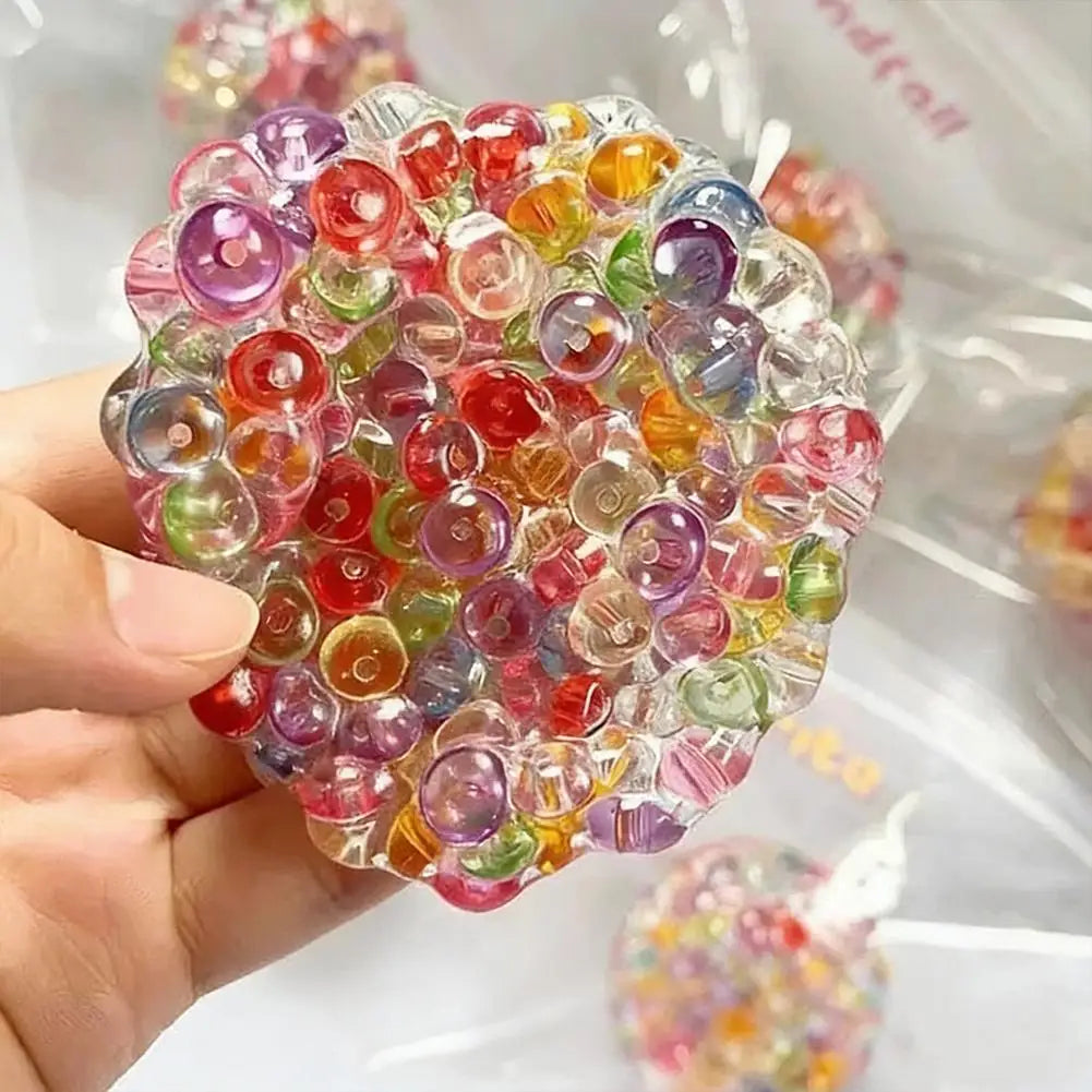 A hand holds a clear, spherical stress ball filled with colorful, translucent beads.