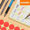 A set of round self-adhesive dot labels in various colors and sizes is shown on a light green pad with a black pen.