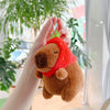 A brown capybara plush toy wearing a red bandana is held by a hand, displayed as a keychain charm.