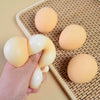 A hand holds a pale yellow squishy hamburger stress ball against a woven mat with other similar balls.