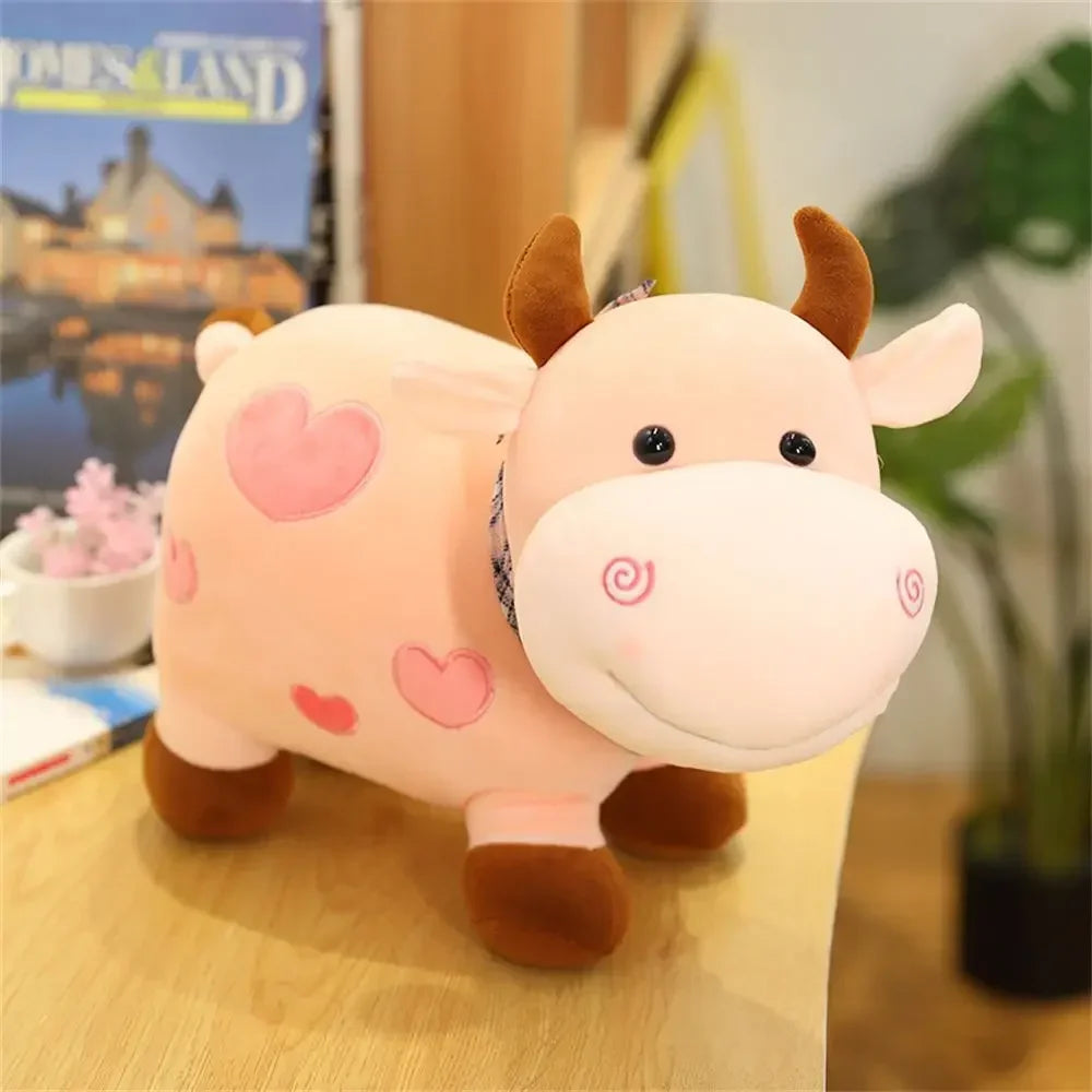 A soft pink and brown cow plush toy with heart accents sitting on a wooden surface.