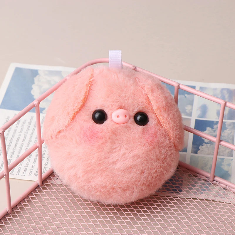 A pink squeaky plush pig keychain with black eyes is displayed inside a pink wire cage.