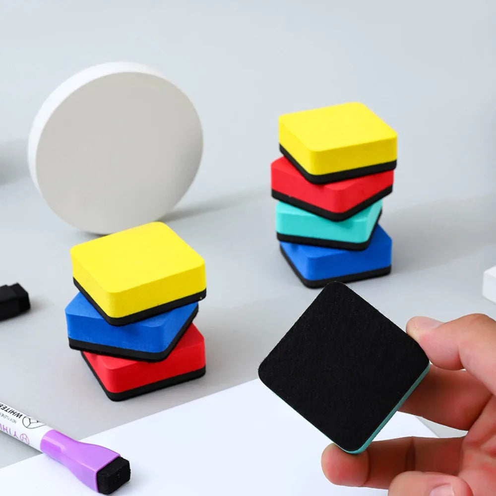 A hand holds a black magnetic whiteboard eraser pad, with two yellow and blue felt pads visible in the background.