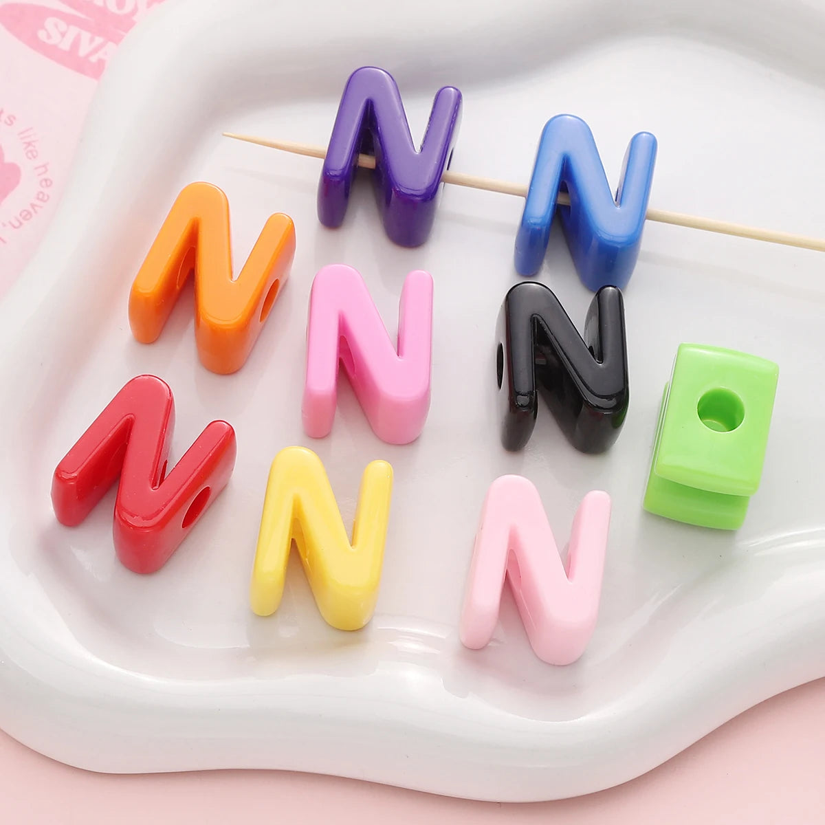 A collection of colorful acrylic letter beads shaped like the letter N arranged on a white tray.