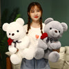 A young woman holds a white teddy bear plush toy with a red rose attached to its collar.