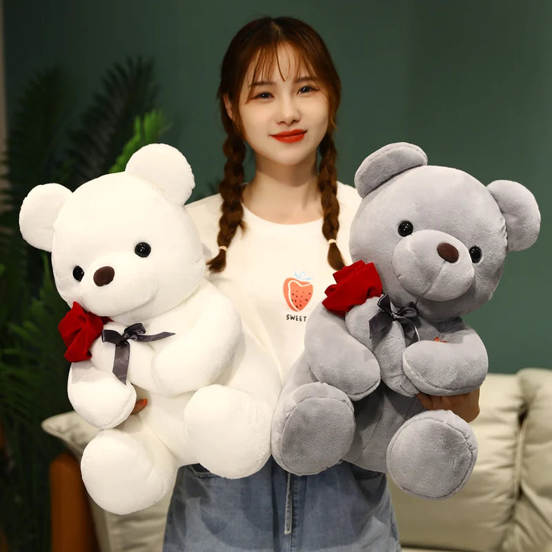 A young woman holds a white teddy bear plush toy with a red rose attached to its collar.