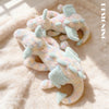 A light pink and mint green rainbow dragon plush toy lying on a fluffy pink surface.
