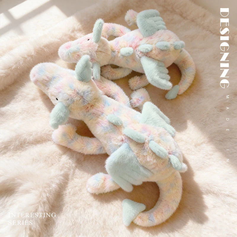 A light pink and mint green rainbow dragon plush toy lying on a fluffy pink surface.