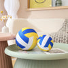 A yellow and blue soft plush volleyball pillow resting on a light green table.