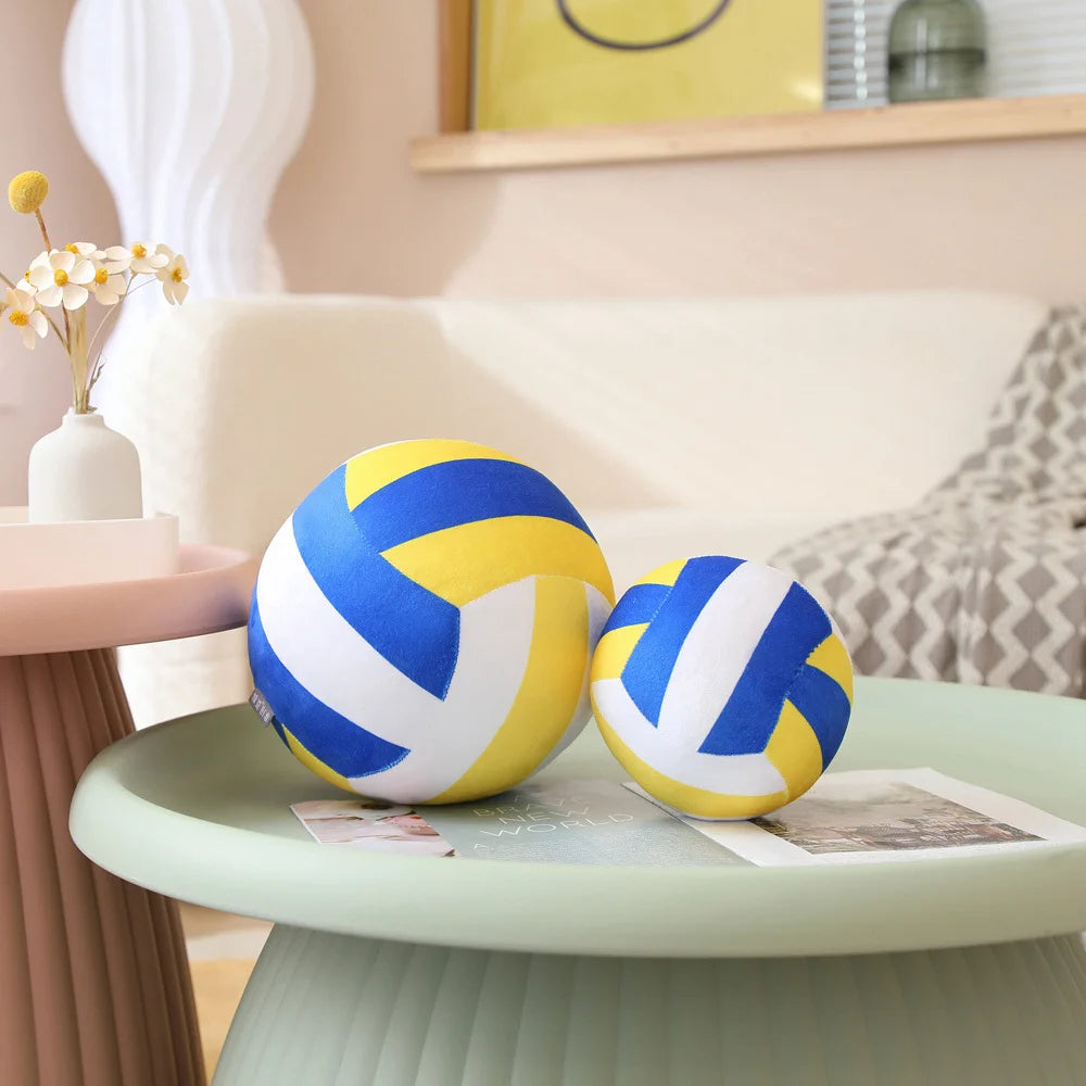 A yellow and blue soft plush volleyball pillow resting on a light green table.