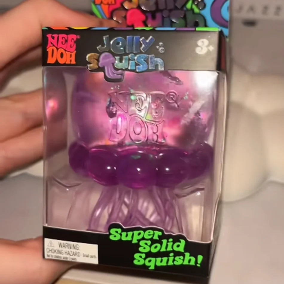 A box of Nee Doh Jelly Squish purple squishy toy with a warning label.