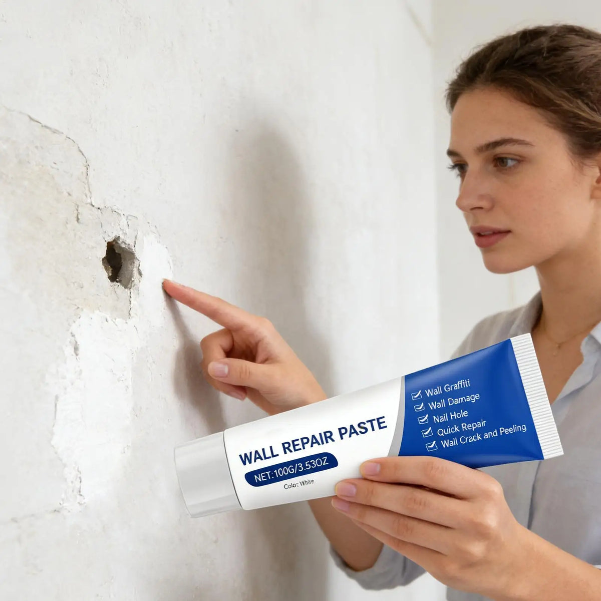 A woman applies white wall repair paste to a damaged white wall surface.